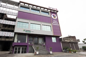 A hotel building with a purple facade, a staircase leading to the entrance, and a sign indicating it is a hotel, banquet, and restaurant. - Treebo Premium Truva (Faridabad)