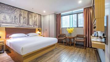 A hotel room with a large bed, a desk with a chair, a small table, and a window with curtains.