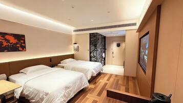 Ein Hotelzimmer mit zwei Betten, einem Schreibtisch, einem an der Wand befestigten Fernseher und einer Tür zu einem weiteren Raum.