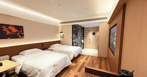 A hotel room with two beds, a desk, a wall-mounted TV, and a door leading to another room.
