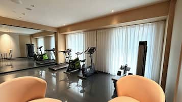 A modern hotel room with a large mirror, exercise equipment, a dining area, and a large window with curtains.