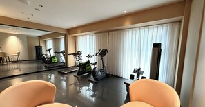 Habitación de hotel moderna con un espejo grande, equipo de ejercicio, zona de comedor y un ventanal con cortinas.