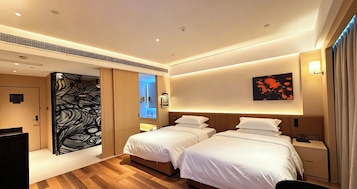 Habitación de hotel con dos camas, un espejo grande, una obra de arte en la pared y piso de madera.