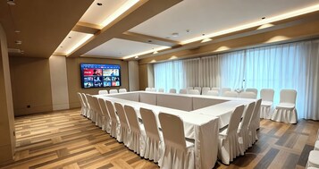 Un salón de conferencias con una mesa larga, sillas, una pantalla grande y vistas al exterior.