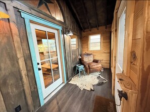 Ein rustikales Interieur mit Holzwänden, einer großen Schiebeglasdoor, einem Ledersessel und einem kleinen Tisch mit Lampe.