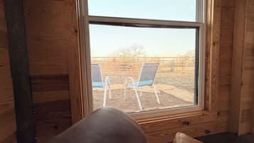 A room with a large window, wooden walls, and two blue chairs outside.