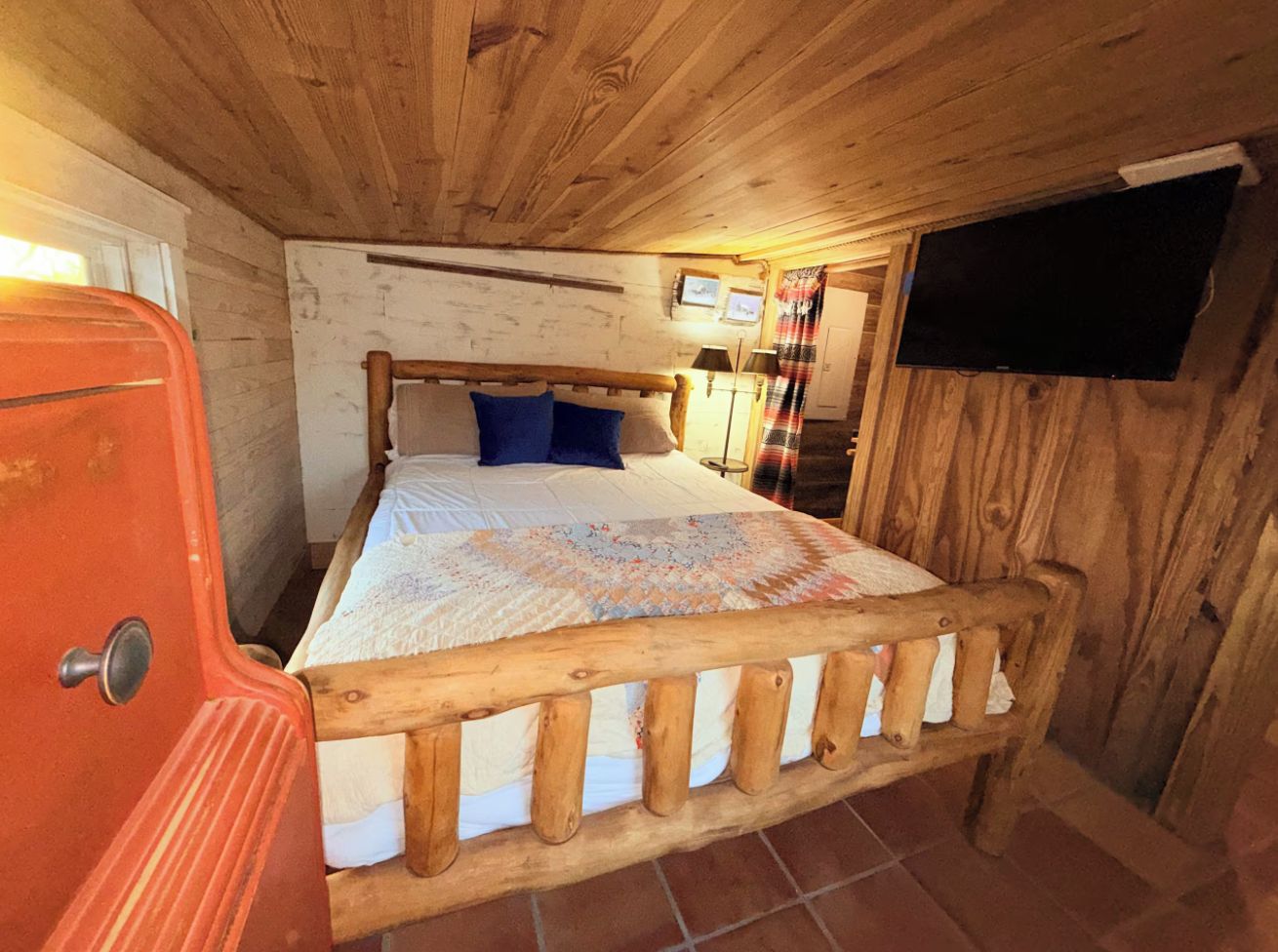 Ein Schlafzimmer mit einem hölzernen Bettgestell, einer Bettdecke und einem Fernseher an der Wand.