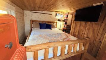 Ein Schlafzimmer mit einem hölzernen Bettgestell, einer Bettdecke und einem Fernseher an der Wand.