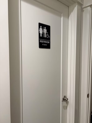 Una porta blanca amb un senyal negre que indica un lavabo per a homes, dones i persones amb mobilitat reduïda.