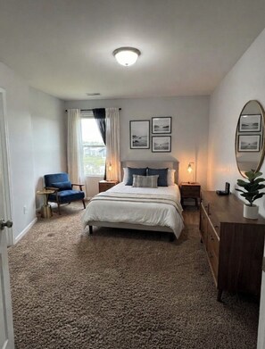 Une chambre à coucher avec un lit, une chaise, une commode, un miroir et des tableaux encadrés accrochés au mur.