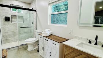 A modern bathroom with a glass shower enclosure, a toilet, a vanity with a sink, and a window.