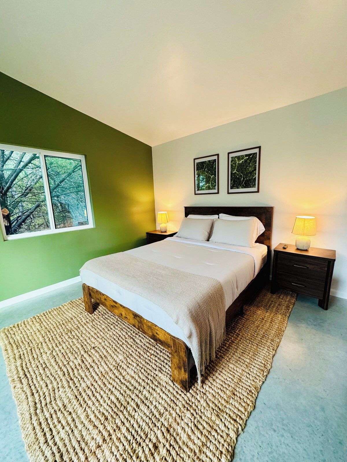 A bedroom with a bed, two bedside tables, a window, and two framed pictures on the wall.
