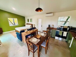 A compact living space with a bed, dining table, chairs, kitchenette, and a view through a window.