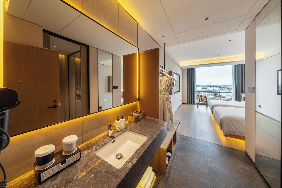 Een moderne hotelkamer met een grote spiegel, een badkamer met wastafel en toilet, een bed en uitzicht op de stad.