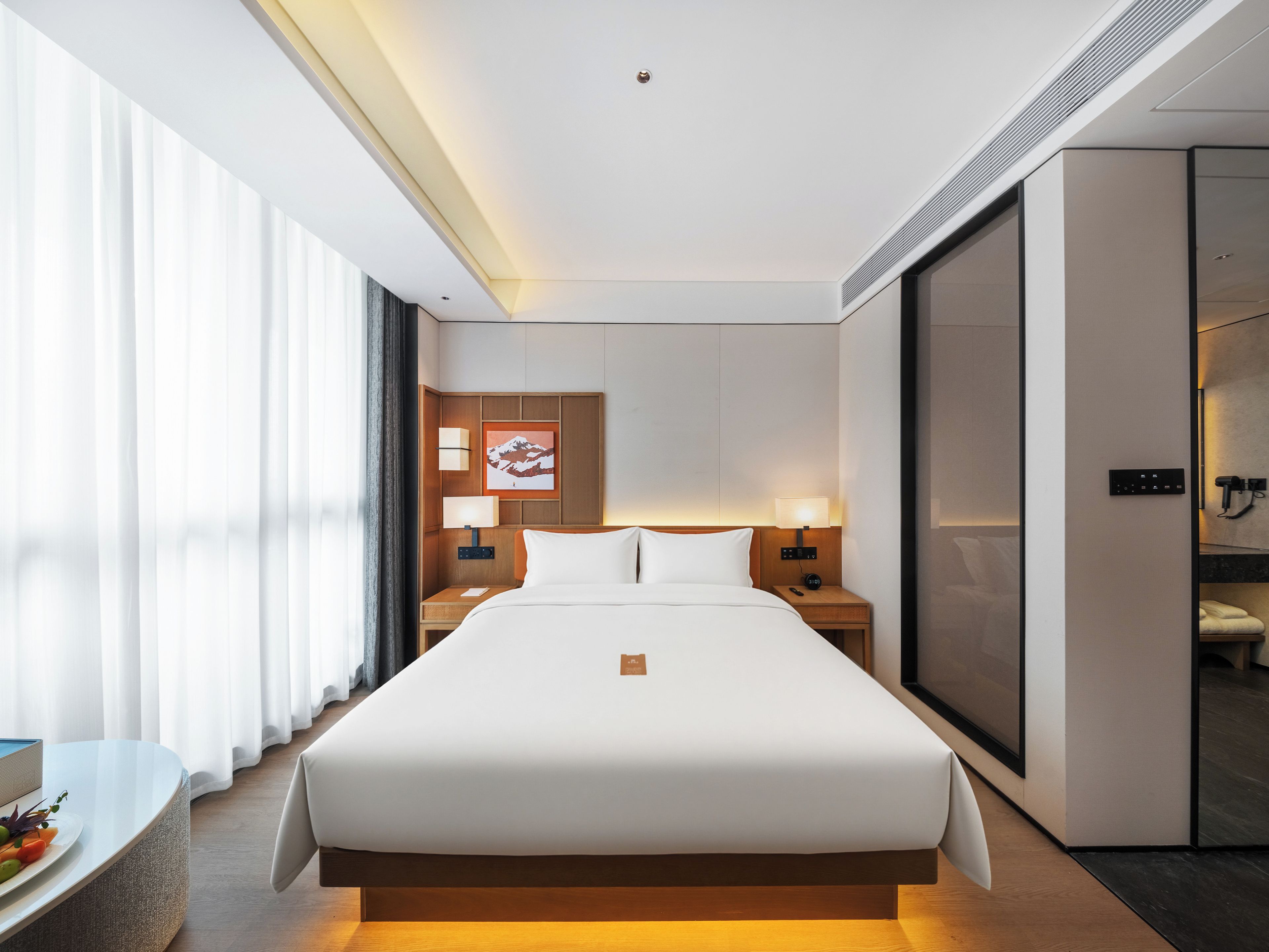 Habitación de hotel con una cama grande, mesitas de noche, un escritorio con una silla, un espejo y una puerta corredera que da a un baño.