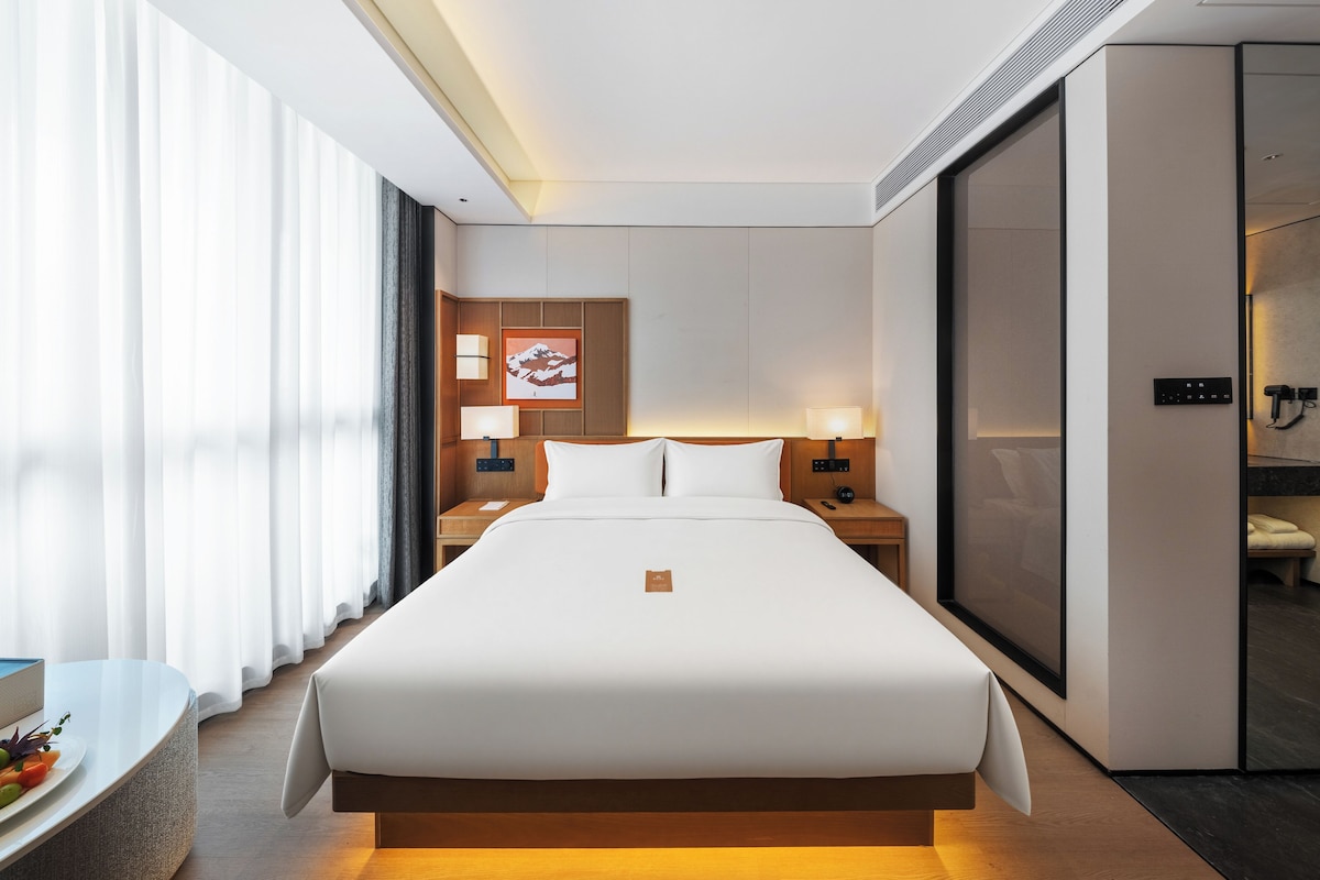 Een hotelkamer met een groot bed, nachtkastjes, een bureau met stoel, een spiegel en een schuifdeur naar een badkamer.