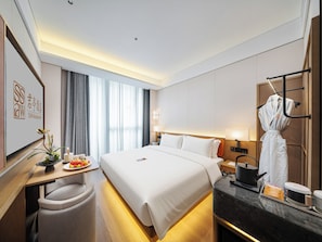 Habitación de hotel con una cama grande, mesitas de noche, un escritorio con silla, una bata colgada en un perchero y vistas al exterior a través de la ventana.