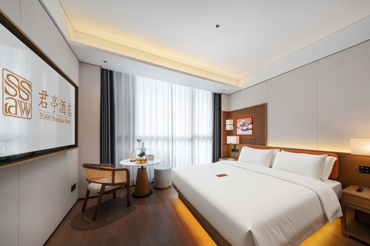 A hotel room with a large bed, a desk, a chair, a small table, and a window with curtains.