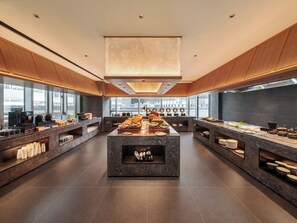 Een modern ontbijtbuffet met een centraal eiland, meerdere aanzitpunten en een groot raam met uitzicht op de stad.