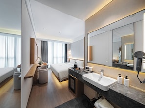 A modern hotel room with a large bed, a sitting area with a table and chairs, a large bathroom with a sink and mirror, and a view of the city through large windows. - SSAW Boutique Hotel Shenzhen Exhibition (Shenzhen)