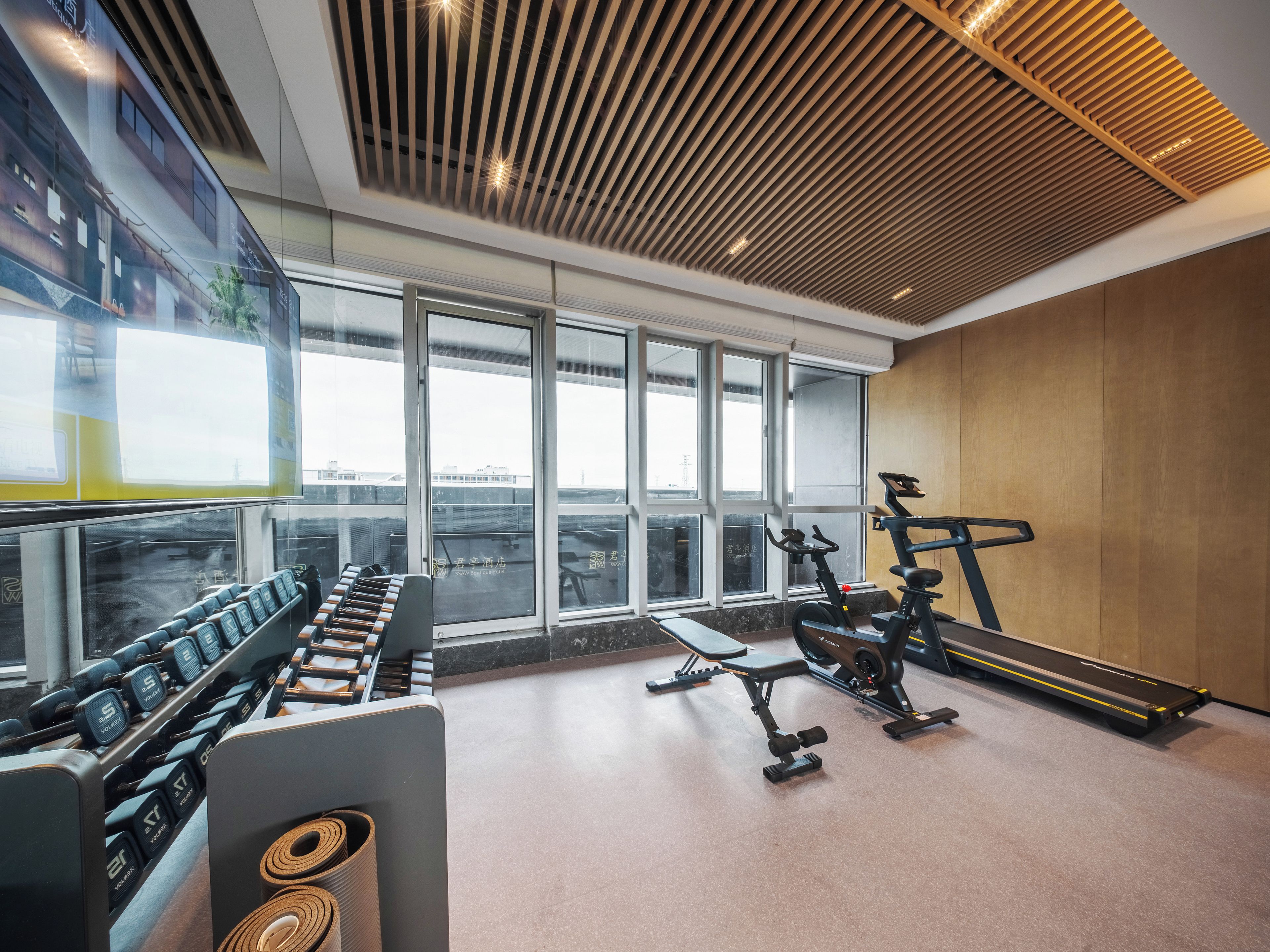 Un gimnasio con equipo de ejercicio, ventanas amplias y techo de madera.