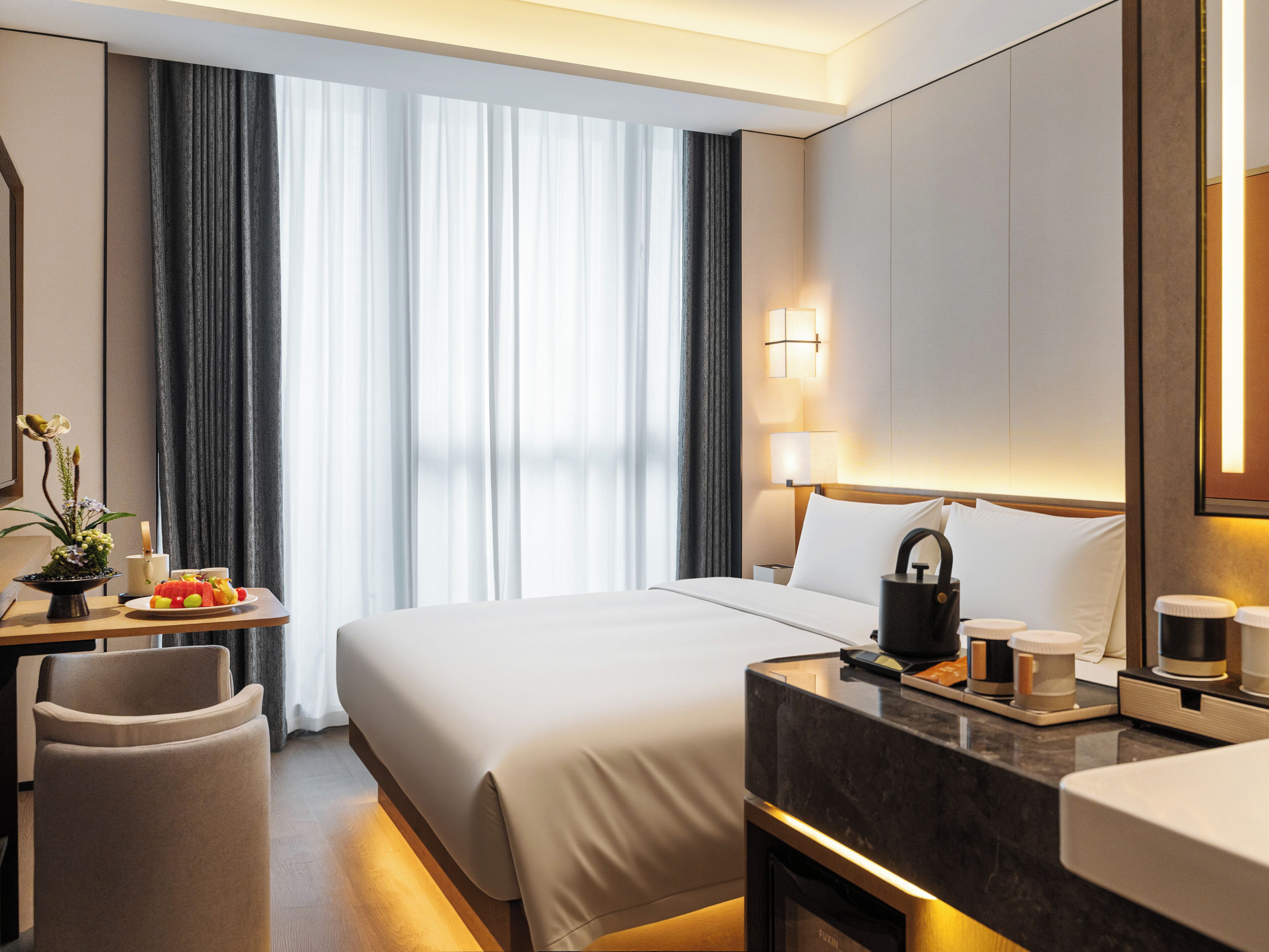 Una habitación de hotel con cama, mesita de noche, lámpara y vistas al exterior a través de la ventana.