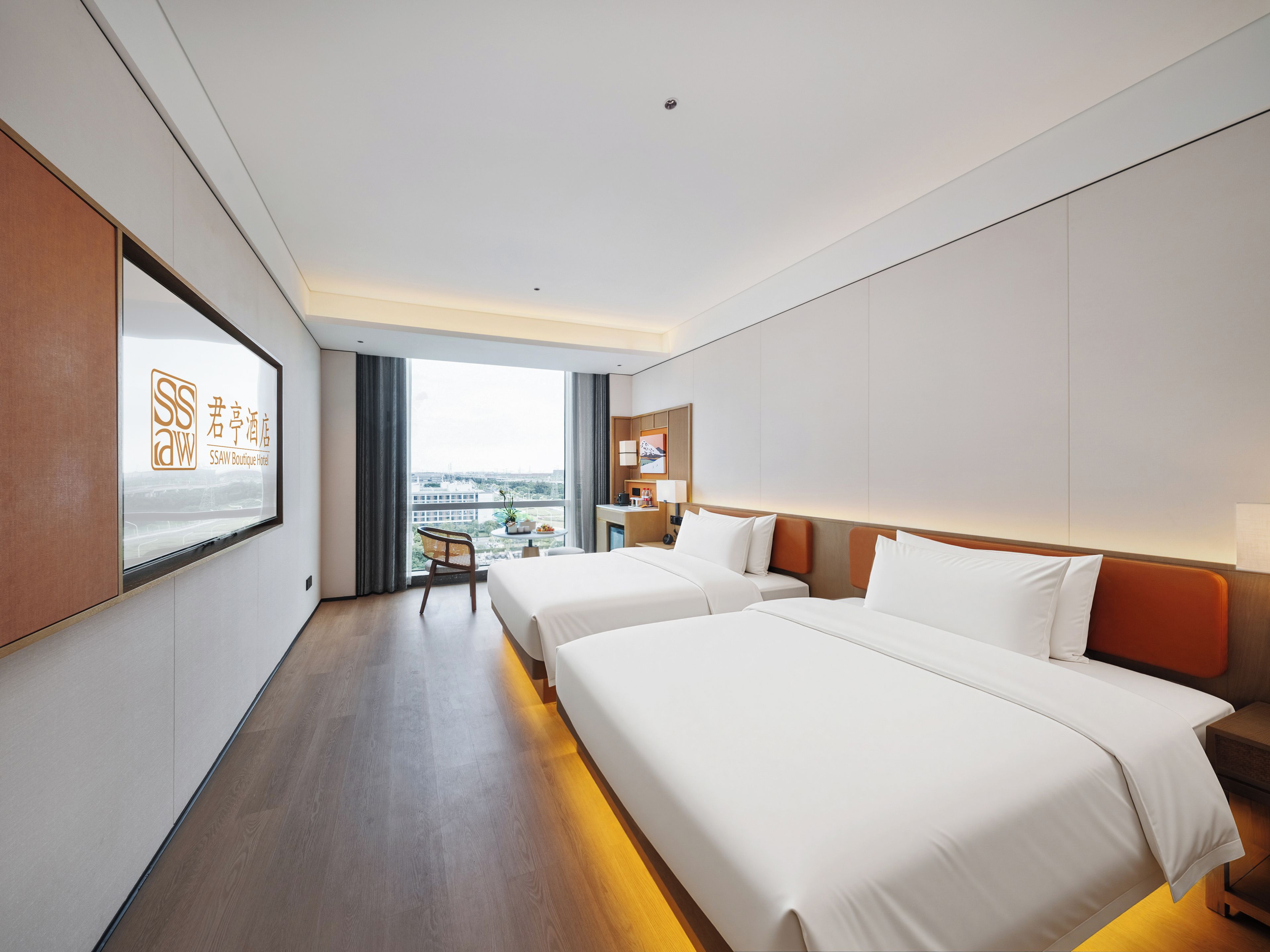 Habitación de hotel con dos camas, un escritorio, una silla y vistas a la ciudad, con un cartel en la pared.