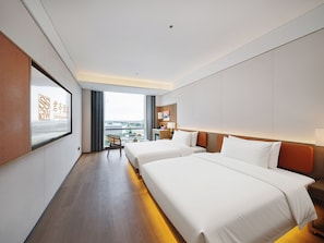 Een hotelkamer met twee bedden, een bureau, een stoel en uitzicht op de stad, met een bord aan de muur.