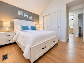 A bedroom with a white bed, two bedside tables with lamps, a white wardrobe, and a door leading to a bathroom. - Immaculate Modern Oasis - Huge Backyard (Mead)