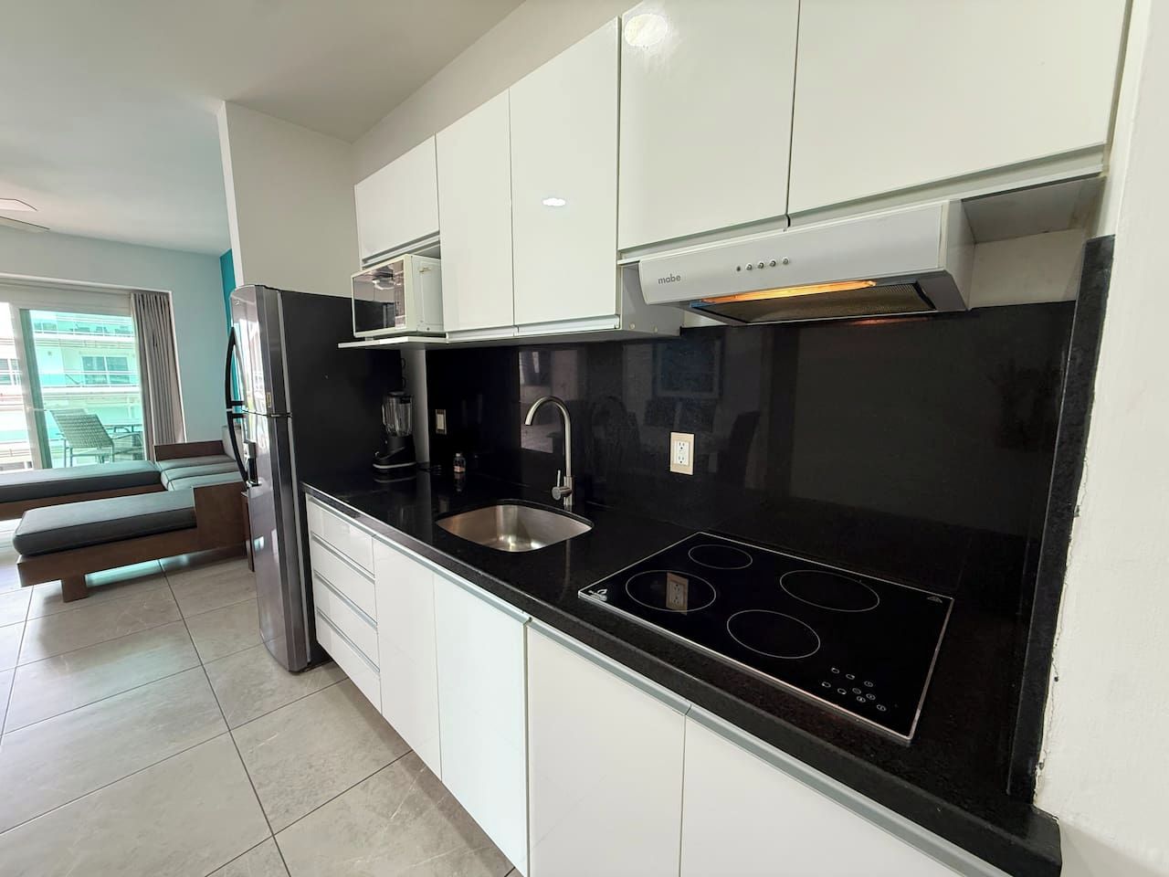 Una cucina moderna con piano di lavoro nero, lavello in acciaio inossidabile e piano cottura integrato.