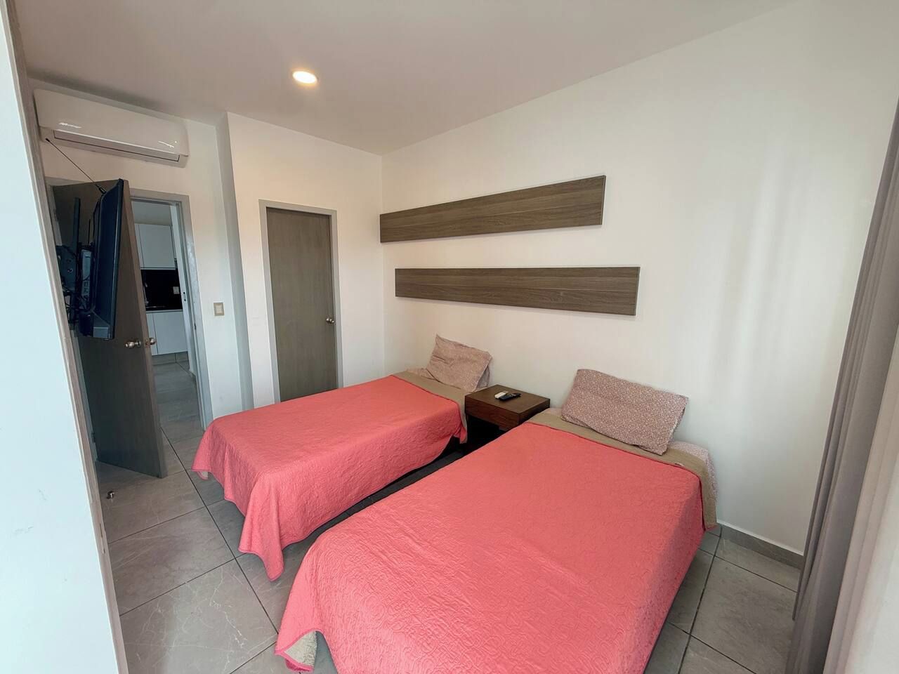Camera d'albergo con due letti, una testiera in legno, un comodino e una porta che dà su un bagno.