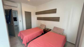 Habitación de hotel con dos camas, un cabecero de madera, una mesita de noche y una puerta que da al baño.
