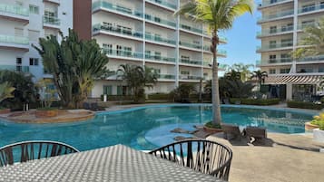 A hotel pool area with a clear blue pool, lounge chairs, and a palm tree.
