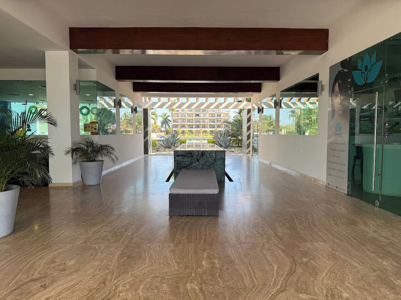 A spacious lobby with a central seating area, potted plants, and a view of a building complex.