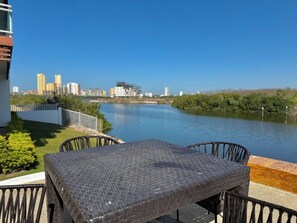 A terrace with a table and chairs overlooking a river, with buildings in the background. - Pacifika, Relax y Lujo Frente a la Marina by GPS (Mazatlán)