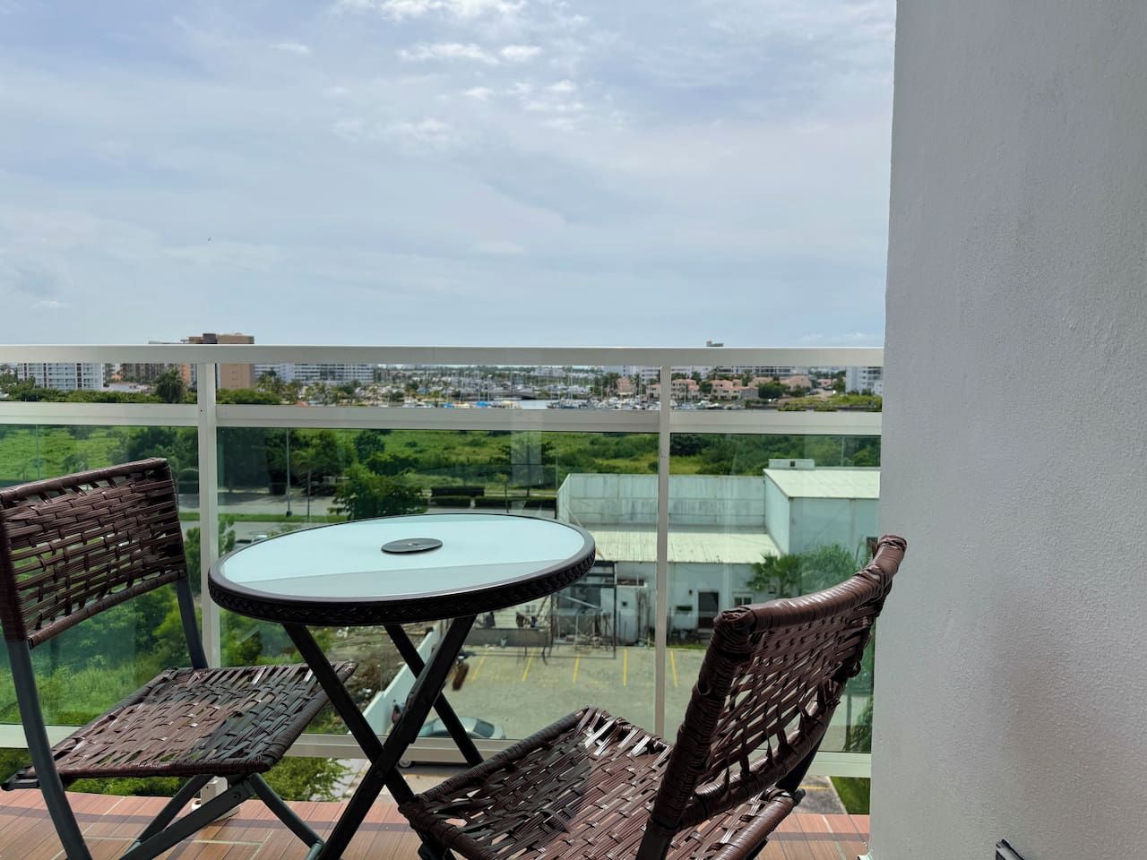 Un balcon avec une table en verre et des chaises en osier, donnant sur un panorama urbain.