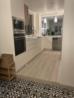 Ett modernt kök med rostfria vitvaror, en träpall och ett golv med mönster.