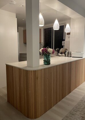 A modern kitchen with a wooden island, pendant lights, and a vase of flowers. - Family Townhouse Randwick (Randwick)