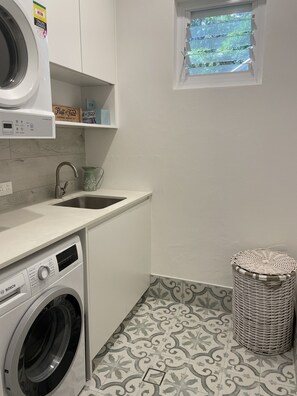 A laundry room with a Bosch washing machine, a sink, and a window with a view of greenery. - Family Townhouse Randwick (Randwick)