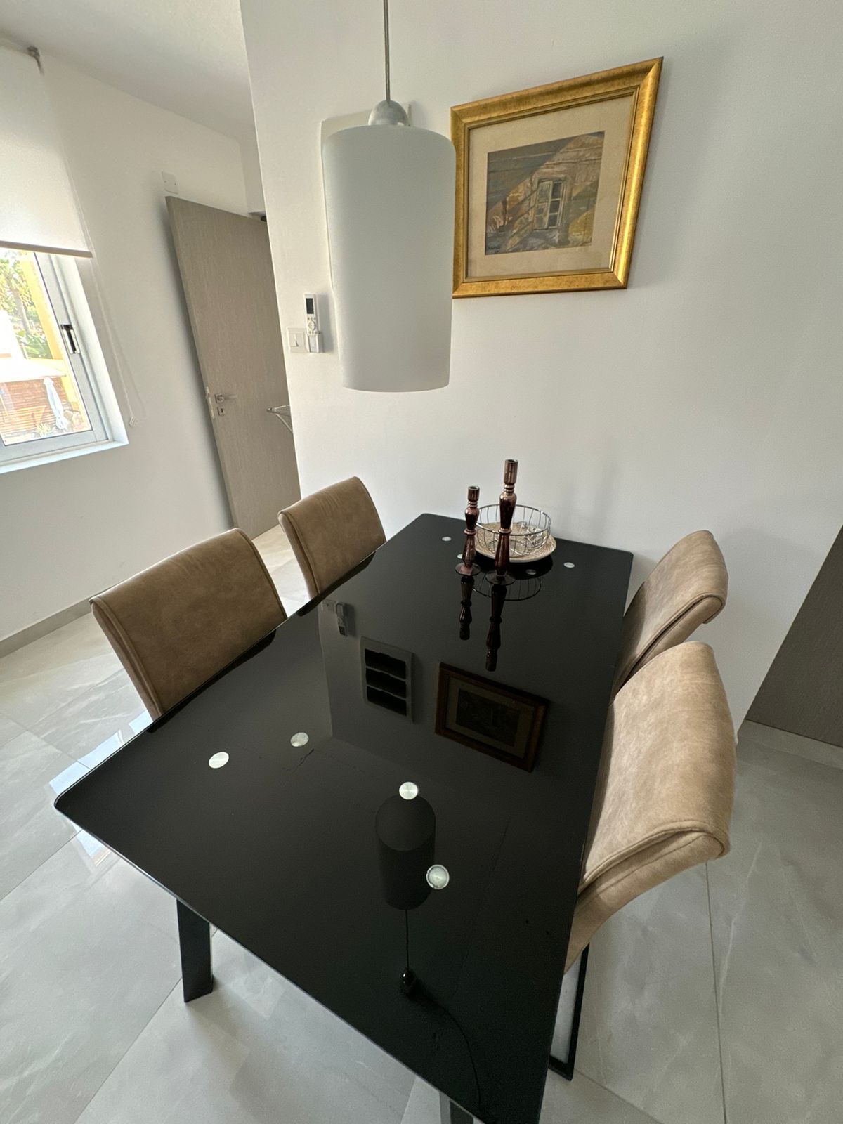 A modern dining area with a black table, cushioned chairs, a pendant light, and a framed picture on the wall.