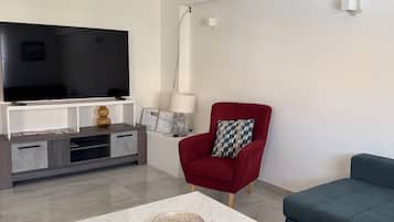 Un salon moderne avec un téléviseur à écran plat, un fauteuil rouge, un canapé bleu et une table basse en marbre.