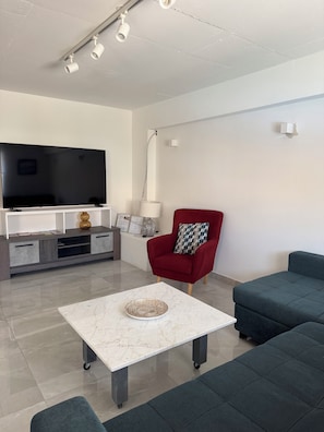 A modern living room with a flat-screen TV, a red armchair, a blue sofa, and a marble coffee table. - Modern 1BR aprt in a Prime Location.Walk everywhere (Pafos)