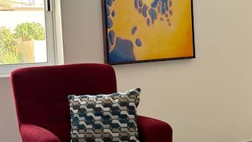 Un fauteuil rouge agrémenté d’un coussin à motifs, une pile de serviettes blanches et un tableau accroché au mur.