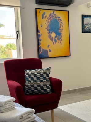 Un fauteuil rouge agrémenté d’un coussin à motifs, une pile de serviettes blanches et un tableau accroché au mur.