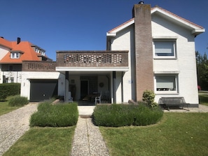 A two-story house with a brick facade, a balcony with a lattice design, and a front porch with a table and chairs. - Zouterik Ground Floor (Cadzand-Bad)