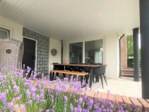 An outdoor patio with a dining table and chairs, surrounded by a garden with purple flowers. - Zouterik Ground Floor (Cadzand-Bad)