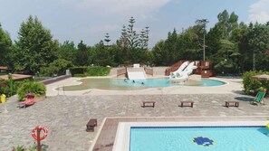 Una piscina amb tobogan, envoltada d'arbres i un salvavides.