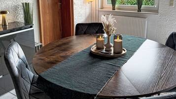 A dining area with a round table, chairs, a vase with dried flowers, and candles.