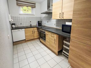 Een kleine keuken met houten kastjes, een ingebouwde oven, een magnetron en een koffiezetapparaat.