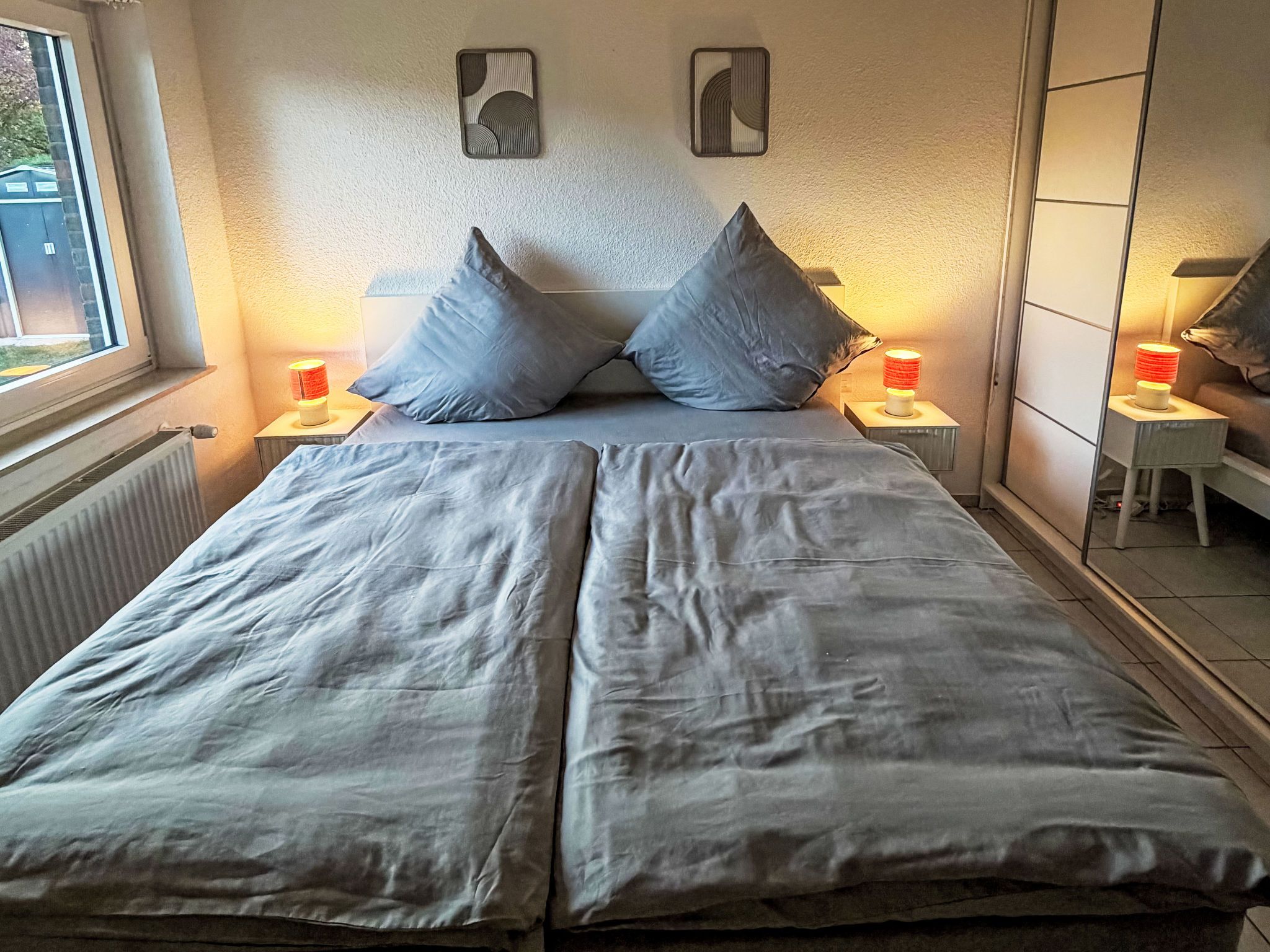 A double bed with two pillows, two bedside tables with lamps, and a radiator.